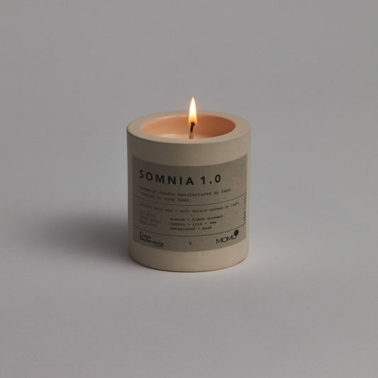 Somnia 1.0 aromatic candle by Momo Cotton with lit flame on gray background