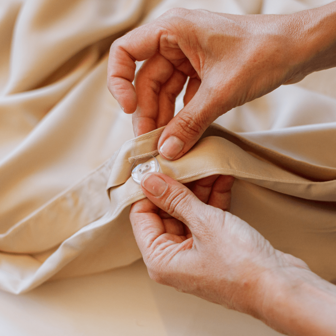 Mains touchant la literie et les serviettes en coton beige doux du set complet Momo Cotton