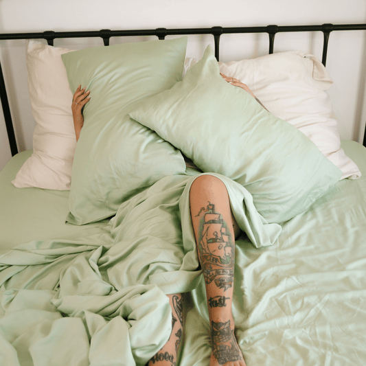Jogo de cama Momo em algodão verde sálvia e branco exibido em cama com cabeceira de metal preto