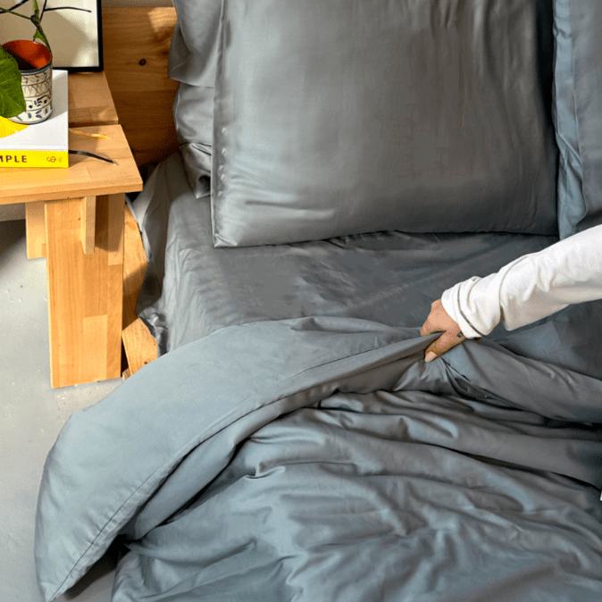 Femme touchant la literie en bambou gris sur le lit avec table en bois en arrière-plan