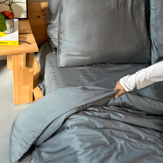 Vrouw aanraakend grijze bamboe beddengoed op bed met houten tafel op de achtergrond