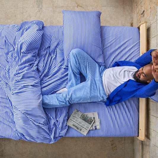 Man slaapt comfortabel op blauw-wit gestreepte bamboe lakens.