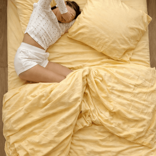 Bed met geel beddengoed en kussen, persoon liggend in decoratieve bedscaping-pose.