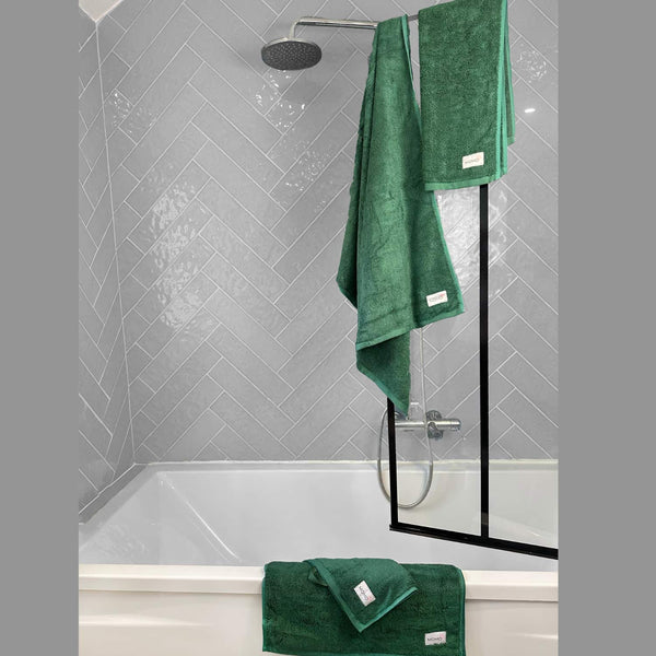 Green Wabi-sabi bath mat displayed in modern shower with herringbone tile walls and black glass enclosure