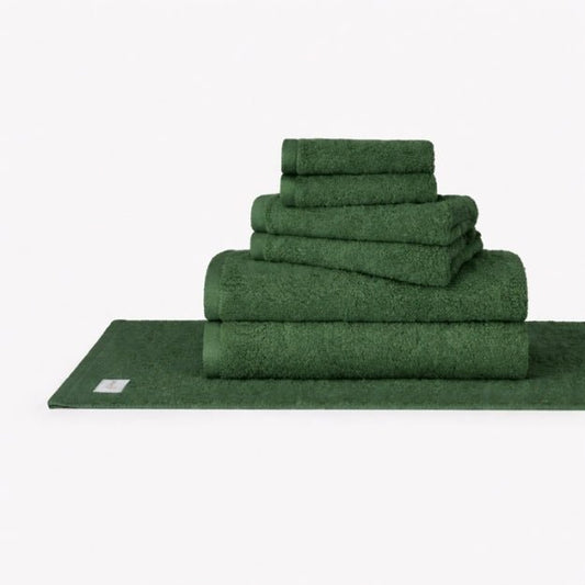 Ensemble de serviettes en coton Wabi Sabi vert empilé affichant serviettes de bain, serviettes de main et gants de toilette sur fond blanc