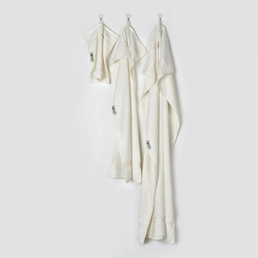 Trois serviettes en bambou crème suspendues à des crochets présentant les tailles visage, main et bain de la collection Alba par momo-cotton