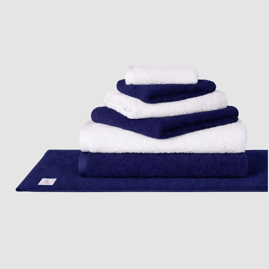 Navy and white Wabi Sabi towel set stacked on navy bath mat against neutral background