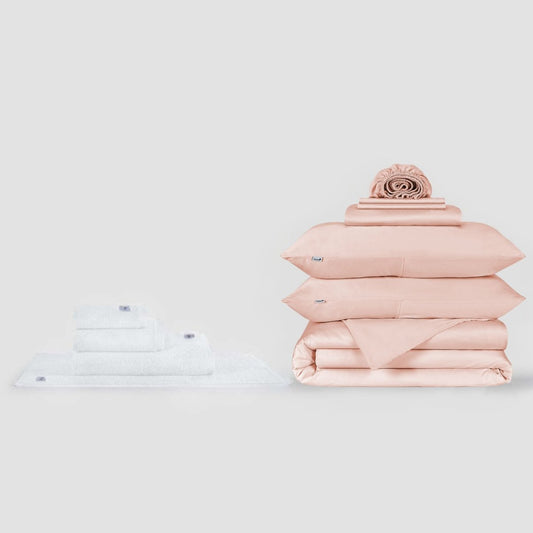 Ensemble de serviettes blanches et parure de lit rose avec coussin décoratif sur fond neutre par Momo Cotton