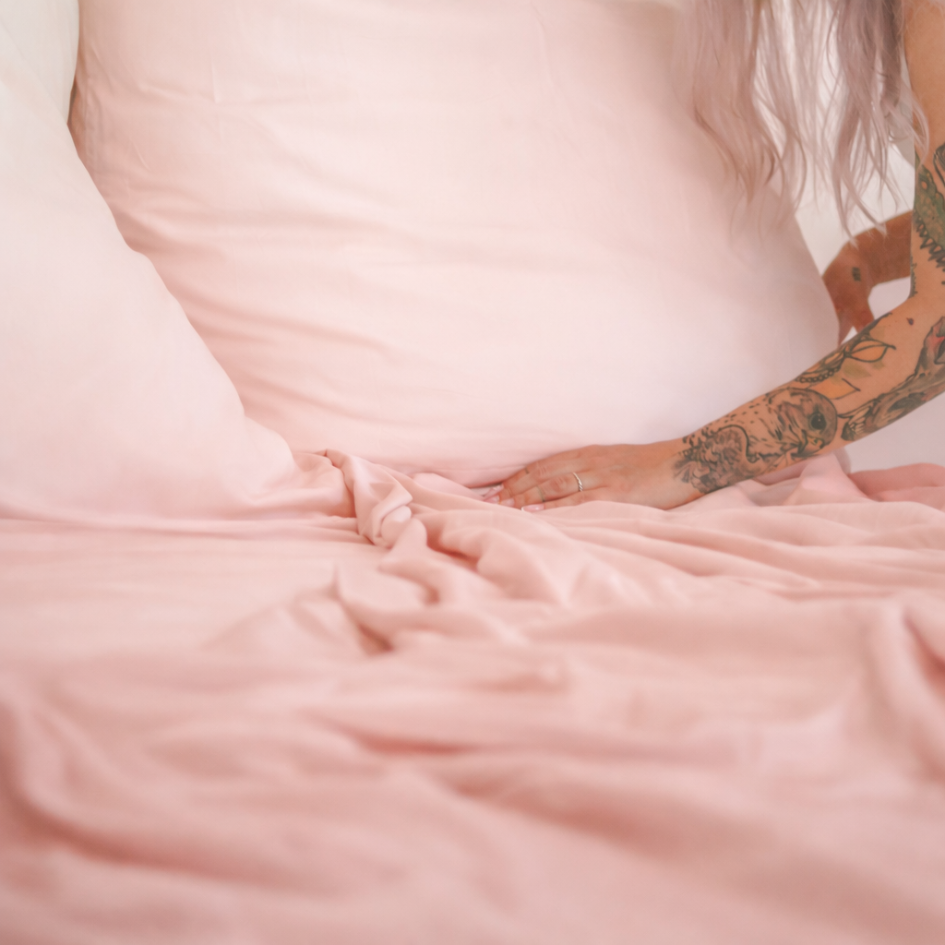 Close-up of a pink bamboe bovenlaken being adjusted over the mattress, showing flexibility and softness.