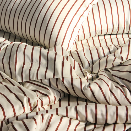 Parure de housse de couette en bambou à motif rayé rouge et beige sur lit défait, texture soyeuse