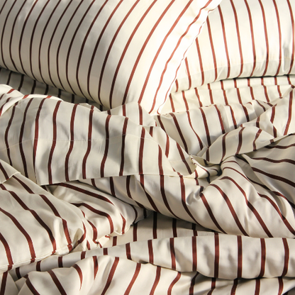 Parure de housse de couette en bambou à motif rayé rouge et beige sur lit défait, texture soyeuse