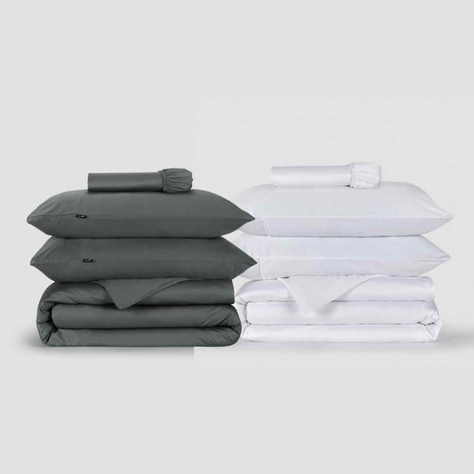 Deux parures de housse de couette Momo Cotton présentées côte à côte, une gris anthracite et une blanche, empilées avec des oreillers