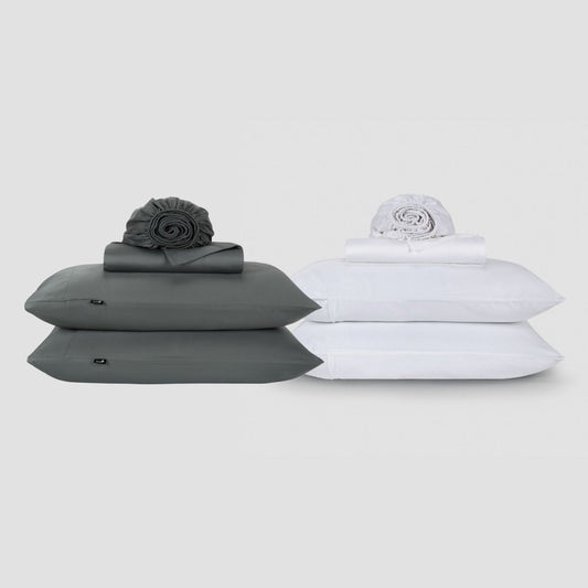 Deux ensembles de draps Momo Cotton côte à côte, un gris anthracite et un blanc, chacun empilé avec des oreillers